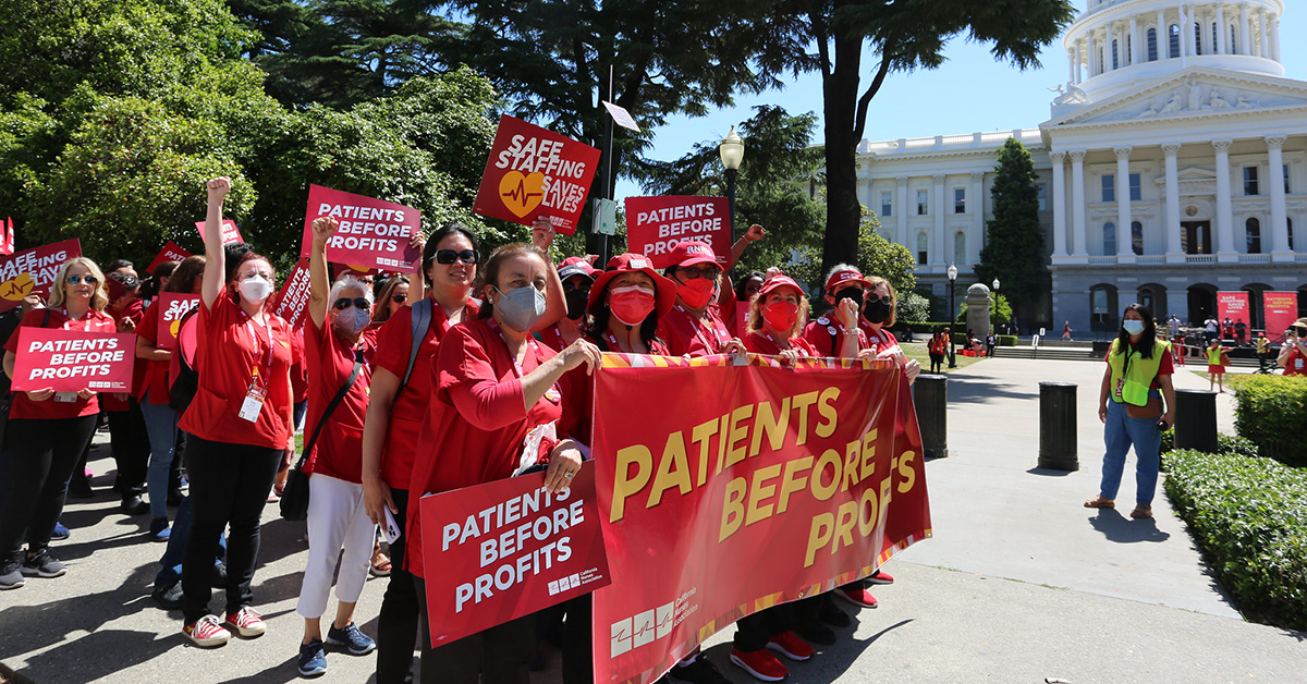 Group of nurses marching towards CA Capitol building, holding banner "Patients over Profits"