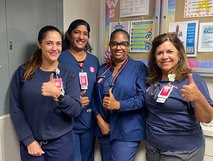 Four nurses inside hospital giving thumbs up